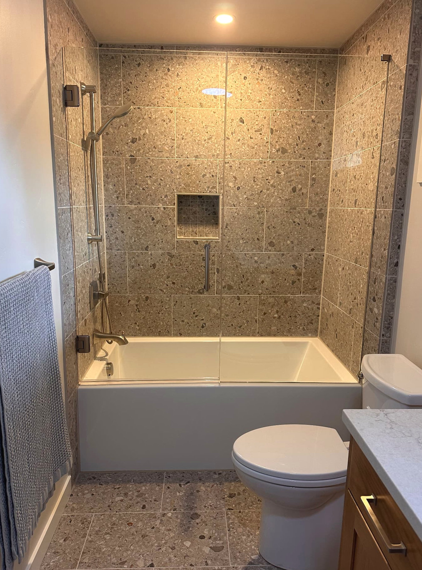 Bathtub with stone-look tile walls, glass screen, and a recessed niche