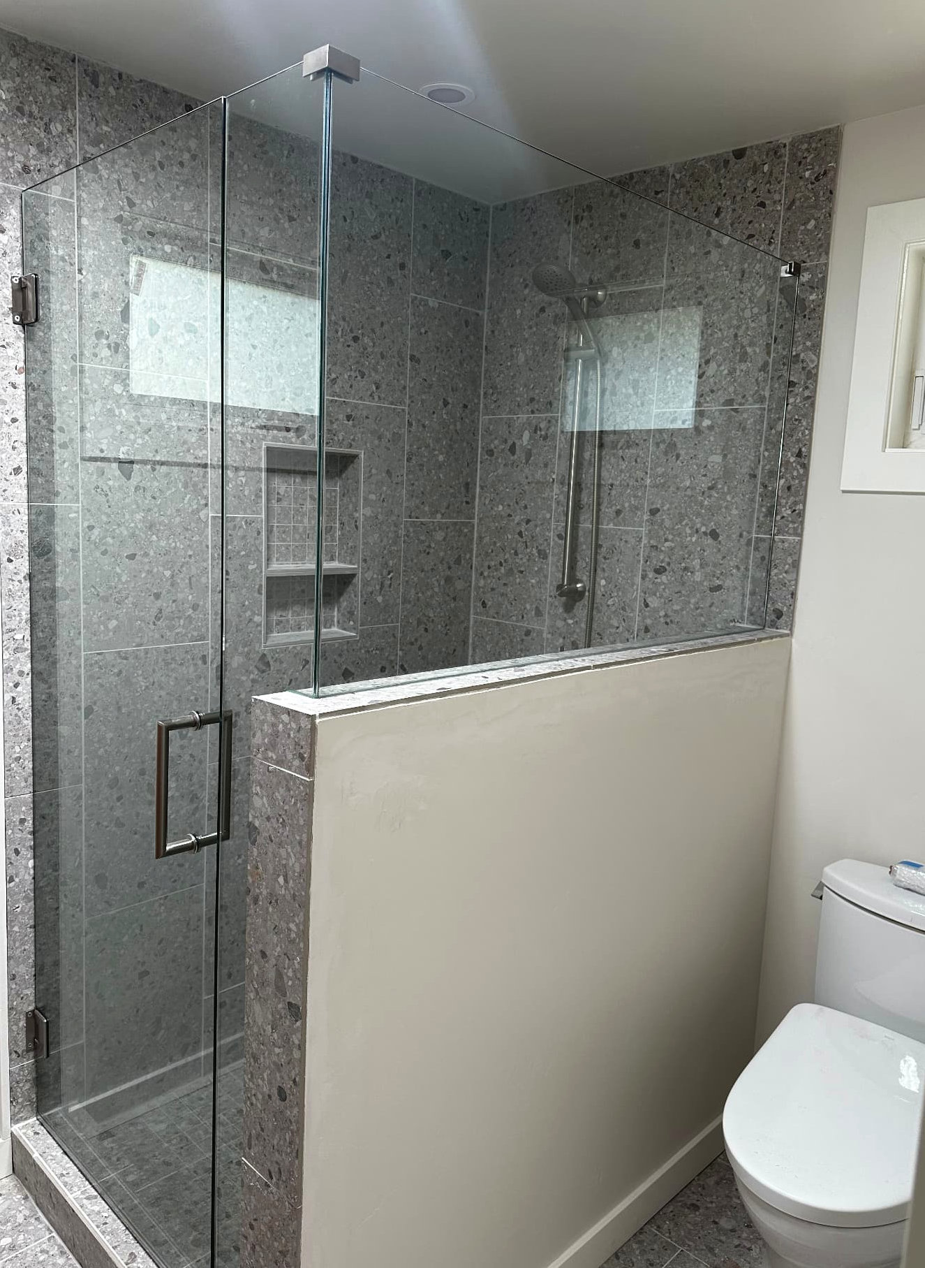 Gray tiled walk-in shower with a glass enclosure and recessed shelving