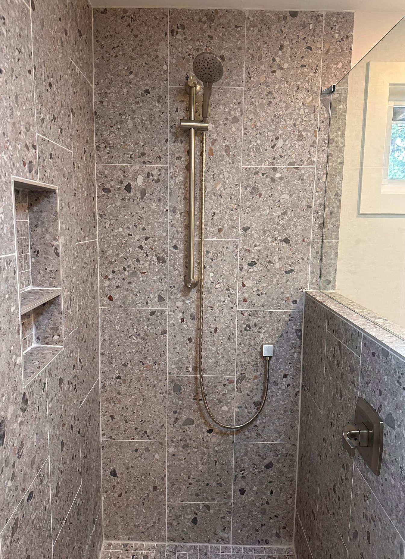 Close view of a tiled shower with a recessed shelf and handheld shower fixture
