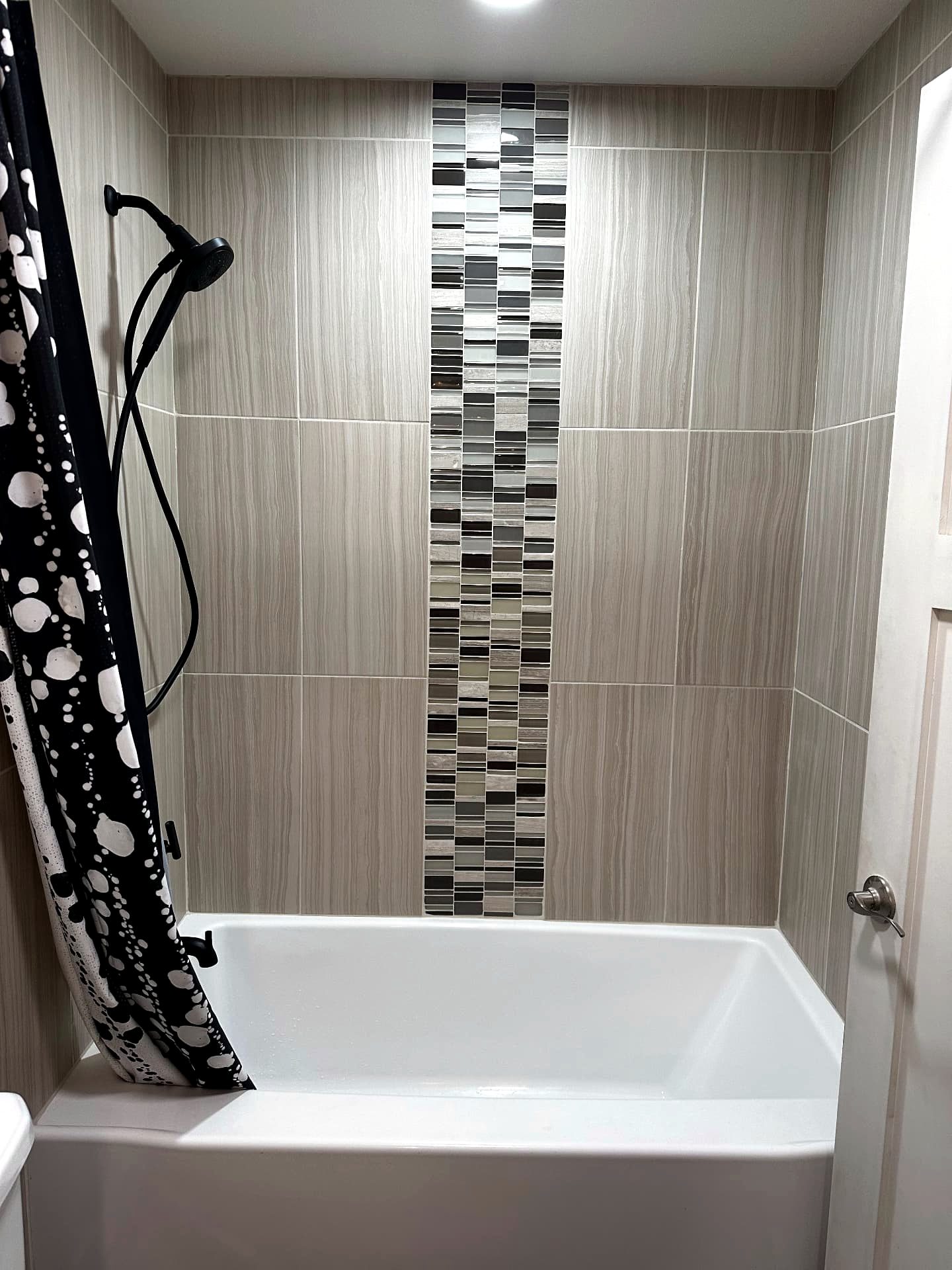 Bathtub with a full-height gray tile surround and a glass mosaic accent strip